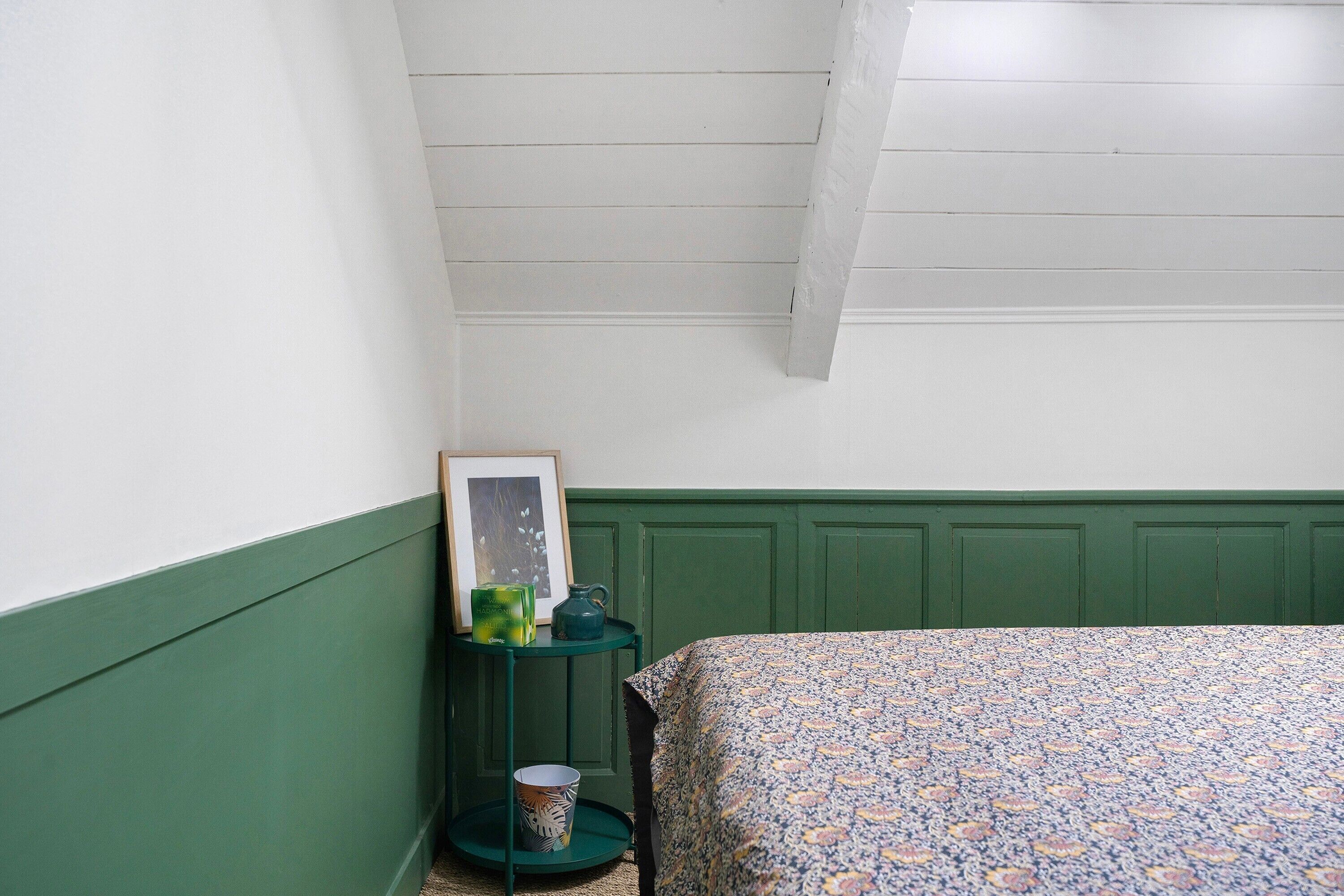 Una camera da letto con pannelli decorativi verdi, una coperta con motivo, un tavolino con una cornice e un lampadario verde.