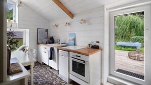 A compact kitchen with white cabinetry, a wooden countertop, a built-in oven, and a view of a garden through a sliding door. - Charming Guest Rooms for a Getaway by the Rance – Cale de Jouvente (Pleurtuit)
