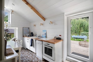 A compact kitchen with white cabinetry, a wooden countertop, a built-in oven, and a view of a garden through a sliding door. - Charming Guest Rooms for a Getaway on the Banks of the Rance - Cale de Jouvente (Pleurtuit)