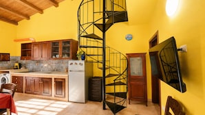 Eine Küche mit Holzschränken, einem weißen Kühlschrank, einer schwarzen Wendeltreppe und einem Essbereich mit Tisch und Stühlen.