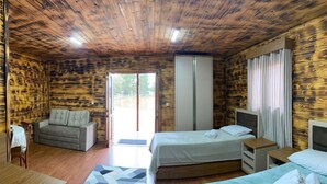 Een kamer met houten wanden en plafond, een bank, twee bedden, een kleine tafel en een raam.