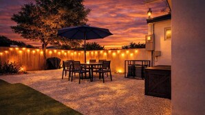Un patio con mesa y sillas, un cerco de madera y luces colgantes.