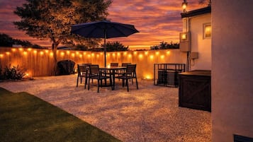 A patio with a table and chairs, a wooden fence, and string lights.