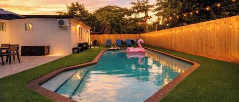 Una piscina con un flotador rosa de flamenco, rodeada por una valla de madera y luces de cuerda.