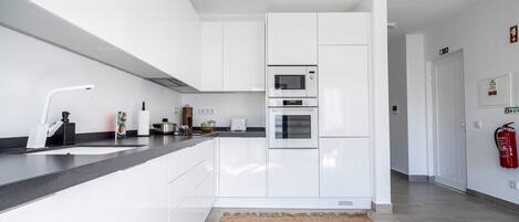 A modern kitchen with white cabinetry, a black countertop, a built-in microwave, and an oven.