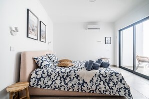 A modern bedroom with a large bed, a small side table, a chair, and a balcony with a view. - Portimao riverview T2 luxe 1st floor with Balcony, Wi-Fi and Air Conditioning (Portimão)