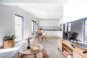 A modern kitchen with white cabinets, a dining area with a round table, and a TV on a stand. - Portimao riverview T2 luxe 1st floor with Balcony, Wi-Fi and Air Conditioning (Portimão)
