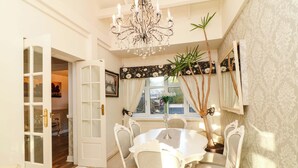 A dining room with a chandelier, white chairs, a round table, and a potted plant. - Ivy's End (Loughborough)