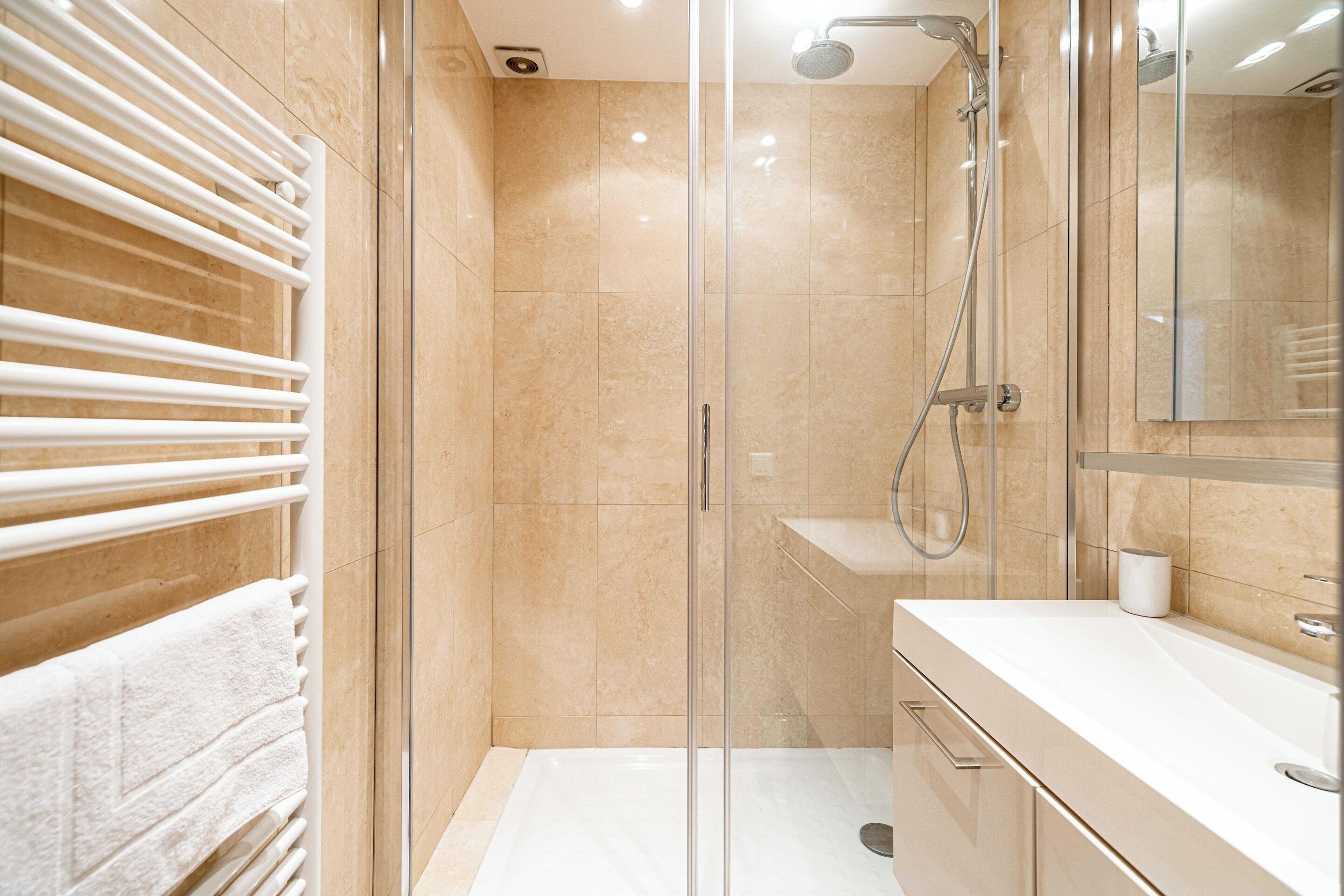 Un bagno moderno con cabina doccia in vetro, un portascopevoli bianco e un mobile vanitario con specchio.