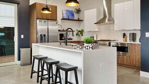 Une cuisine moderne dotée d’un îlot central, de tabourets de bar, d’appareils électroménagers en acier inoxydable et de luminaires suspendus.