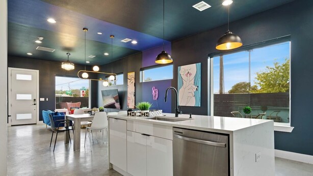 Une cuisine moderne dotée d’un îlot central, de luminaires suspendus et de grandes fenêtres offrant une vue sur l’extérieur.