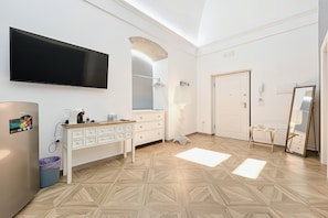 A modern bedroom with a flat-screen TV, a vanity with a mirror, a wooden floor, and a door. - Queen Room 'Orchidea Celeste' with Sea View, Wi-Fi, and Air Conditioning (Manfredonia)