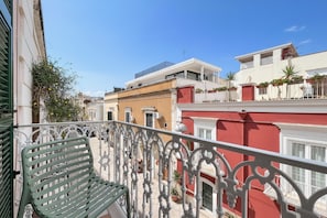 A balcony with a green metal bench, white ornate railing, and a view of adjacent buildings with balconies and potted plants. - Queen Room 'Orchidea Celeste' with Sea View, Wi-Fi, and Air Conditioning (Manfredonia)