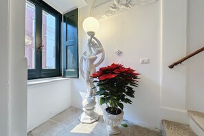 A hallway with a white statue, a potted plant with red flowers, a door with a black frame, and a staircase. - Triple Room 'Orchidea Celeste' with Sea View, Wi-Fi and Air Conditioning (Manfredonia)