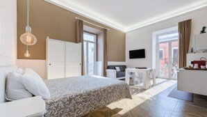 A hotel room with a bed, a desk, a chair, a TV, and a balcony with curtains. - Triple Room 'Orchidea Celeste' with Sea View, Wi-Fi and Air Conditioning (Manfredonia)