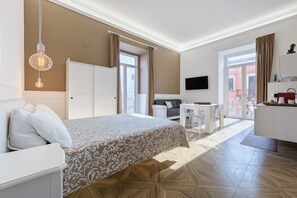 A hotel room with a bed, a desk, a chair, a TV, and a balcony with curtains. - Triple Room 'Orchidea Celeste' with Sea View, Wi-Fi and Air Conditioning (Manfredonia)