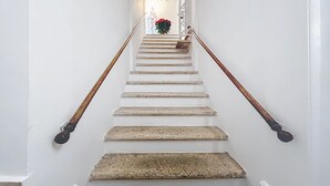 A staircase with white walls, wooden handrails, and a floral arrangement at the top. - Triple Room 'Orchidea Celeste' with Sea View, Wi-Fi and Air Conditioning (Manfredonia)