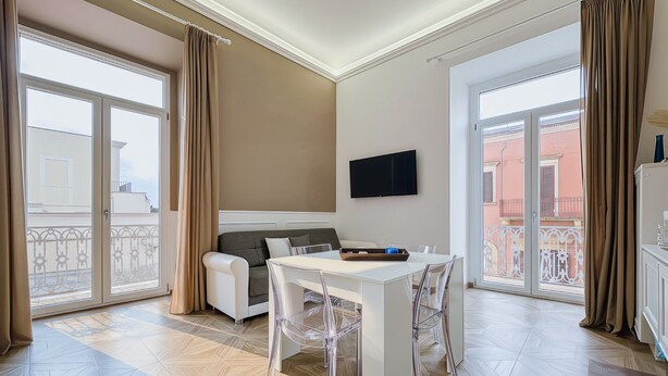 A spacious room with a dining table, clear chairs, a sofa, and a TV mounted on the wall. - Triple Room 'Orchidea Celeste' with Sea View, Wi-Fi and Air Conditioning (Manfredonia)
