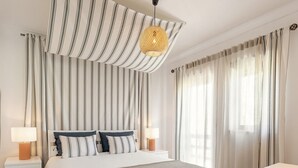 A neatly arranged bedroom with a bed, bedside tables, a hanging light fixture, and a view of the outdoors through curtains.