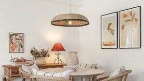 A dining area with wicker chairs, a round table, a hanging light fixture, and framed artwork on the wall.