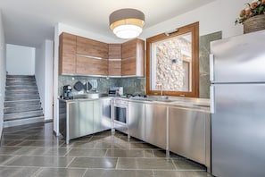 A modern kitchen with stainless steel appliances, wooden cabinets, a stone backsplash, and a built-in oven. - Villa Altamarea - Scopello (Scopello)