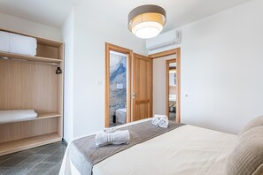 A bedroom with a bed, a wooden wardrobe, a bathroom visible through an open door, and a ceiling light fixture. - Villa Altamarea - Scopello (Scopello)