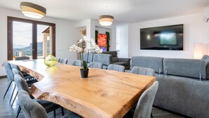 A modern dining area with a wooden table, grey upholstered chairs, and a large flat-screen TV mounted on the wall. - Villa Altamarea - Scopello (Scopello)