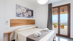 A hotel room with a bed, a bedside table, a telephone, a painting, and a view through the door. - Villa Altamarea - Scopello (Scopello)