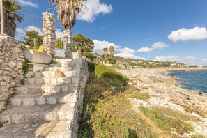 A coastal stone staircase leading down to a beach, with a clear view of the sea and a few palm trees in the background. - Il Nido Delle Onde - Marina Di M... (Marina di marittima)