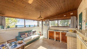 Une cuisine chaleureuse, aménagée dans le style d’un chalet, avec un plafond en bois, un coin repas comprenant une table et des chaises, un canapé et une vue sur la mer grâce à de grandes fenêtres.