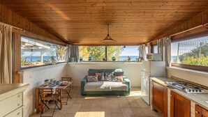 Une cuisine chaleureuse avec un plafond en bois, un coin repas avec une table et des chaises, un canapé et une vue sur la mer grâce à de grandes fenêtres.