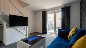 Ein modernes Wohnzimmer mit einem blauen Sofa, einem flachbildfernseher, der an einer weißen Wand angebracht ist, und einer Glastür, die zu einem Außenbereich führt.