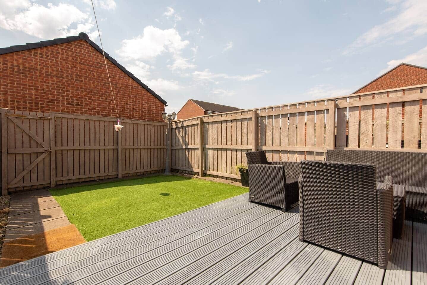 A backyard with a wooden deck, a green lawn, and a brick wall.