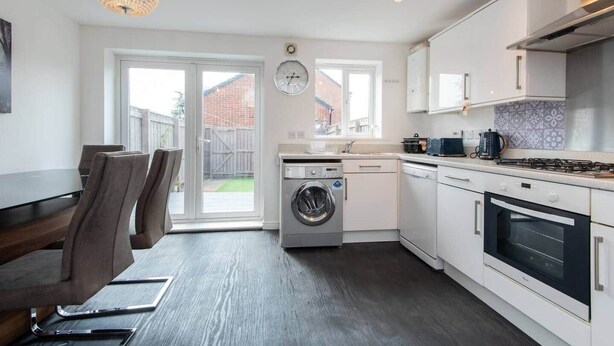 Eine moderne Küche mit Waschmaschine, Backofen und Essbereich mit Stühlen.