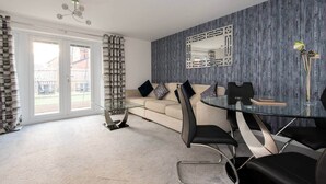 Un salón moderno con una mesa de comedor de vidrio, sillas negras, un sofá beige y un ventanal con cortinas.