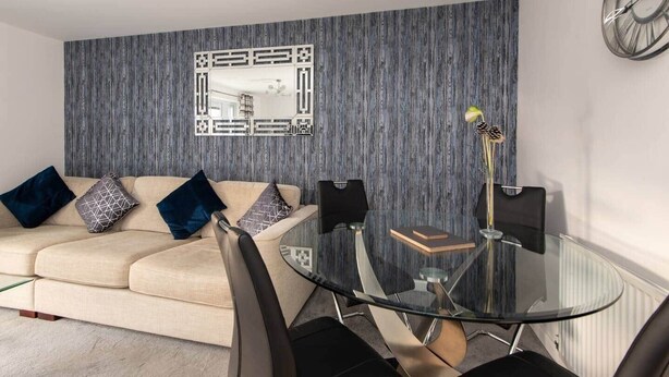 Una sala de estar moderna con un sofá, una mesa de comedor de vidrio y un espejo decorativo en la pared.