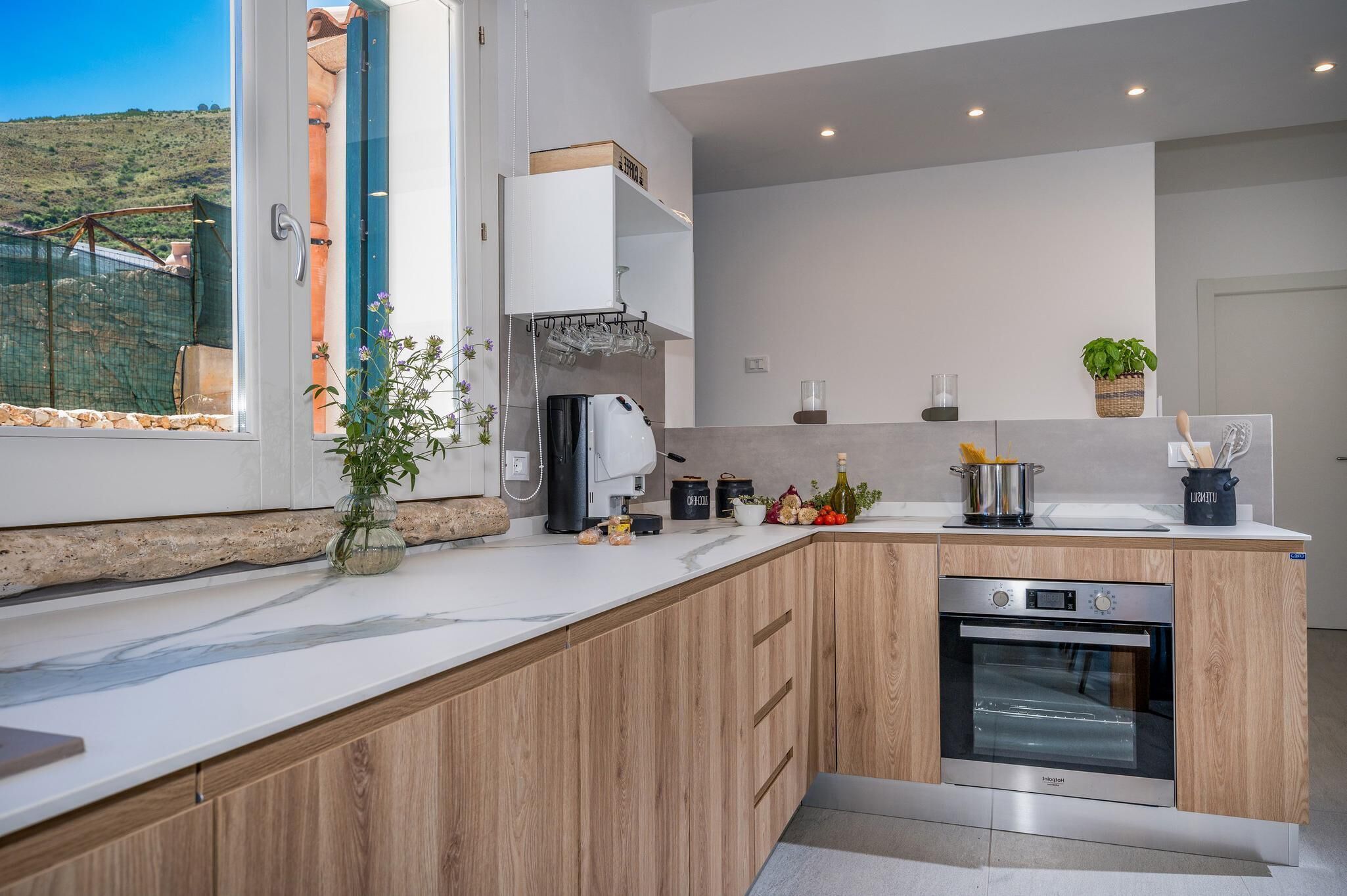 Una cocina moderna con armarios de madera, horno integrado y ventana con vista a un jardín.