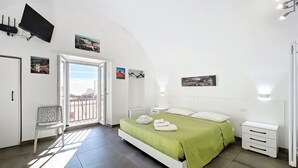 A bedroom with a bed, a chair, a TV, and artwork on the walls. - Casa Veroncelli Apartment with Sea View, Balcony and Wi-Fi (Monte SantʼAngelo)