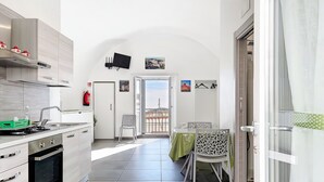 A modern kitchen with a stove, oven, and sink, a dining area with a table and chairs, and a view of the outside. - Casa Veroncelli Apartment with Sea View, Balcony and Wi-Fi (Monte SantʼAngelo)