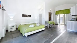 A bedroom with a bed, bedside tables, a chair, a table, and a kitchenette. - Casa Veroncelli Apartment with Sea View, Balcony and Wi-Fi (Monte SantʼAngelo)