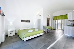A bedroom with a bed, bedside tables, a chair, a table, and a kitchenette. - Casa Veroncelli Apartment with Sea View, Balcony and Wi-Fi (Monte SantʼAngelo)