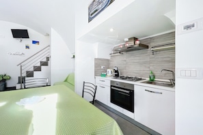 Une cuisine moderne dotée d’une cuisinière, d’un four et d’un évier intégrés, un coin repas avec une table et des chaises vertes, et un escalier muni d’une main courante.