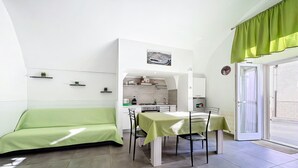 Een ruimtelijk ingerichte leefruimte met kitchenette, een eethoek en een groene bank.