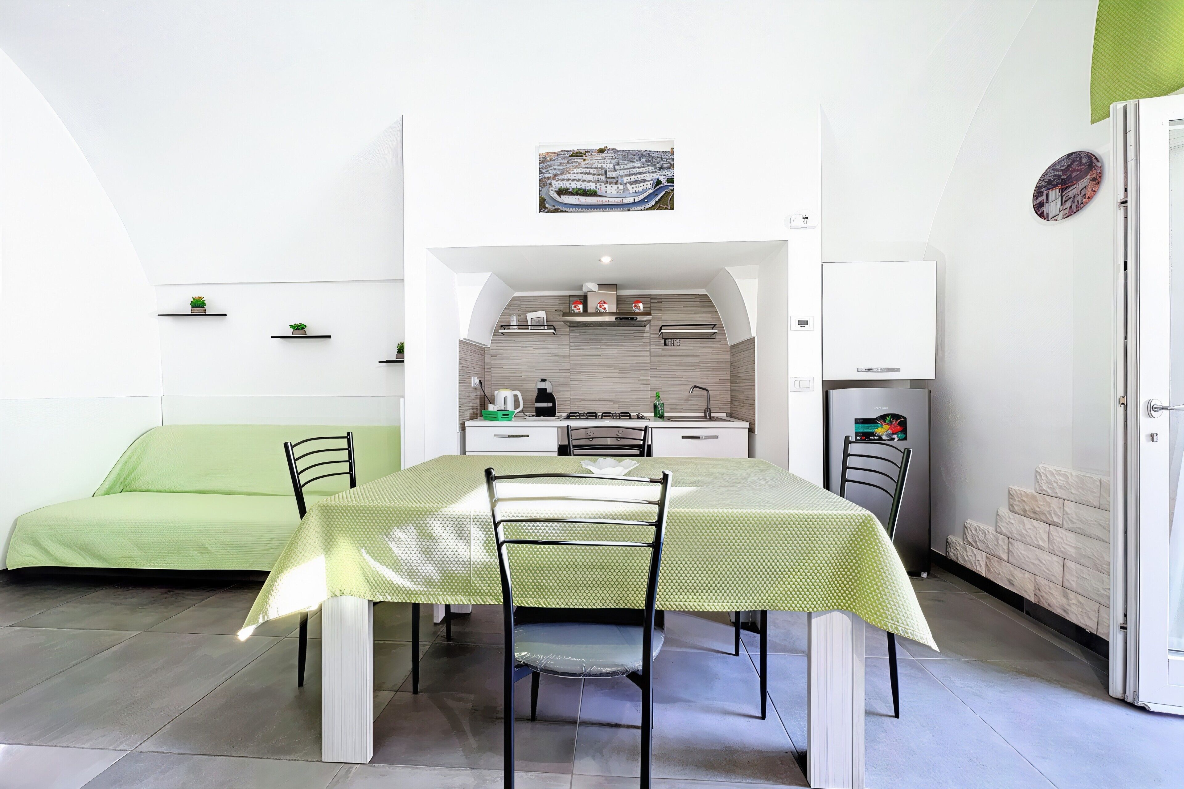 Un ambiente compatto con angolo pranzo, angolo cottura e divano verde.