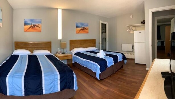 Een hotelkamer met twee bedden, een kleine kitchenette en een deur naar een andere kamer.