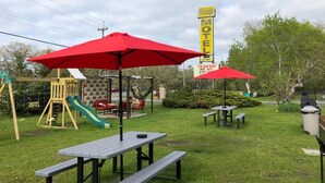 Een park met picknicktafels, rode parasols, een speeltuin en een motelbord.