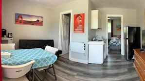 Een compacte hotelkamer met een kitchenette, een eethoek met een tafel en stoelen, een bed en een televisie.