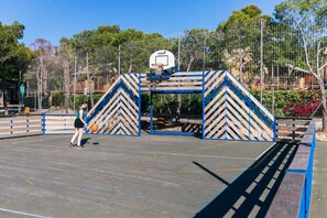 An outdoor basketball court with a blue and white chevron-patterned structure, a basketball hoop, and a person playing. - Good Standard Furnished Chalet on Nice Park (Castellet i la Gornal)