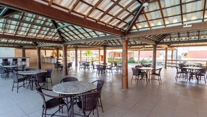 Un espace extérieur aménagé en terrasse, avec plusieurs tables et chaises, une structure de toit abritée et une vue sur les bâtiments environnants.