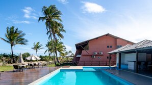 Une piscine avec une terrasse carrelée, des palmiers et un bâtiment à la façade rouge.